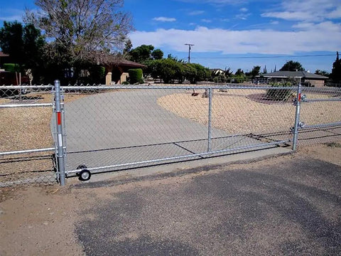Heavy Duty Galvanized Steel Rolling Gate Hardware Kit With Slick 6 Inch Double Track Wheels and Six Wall Mount Brackets Plus Solid Rolo Latch For Chain Link Sliding Gates, installed on a gravel driveway.