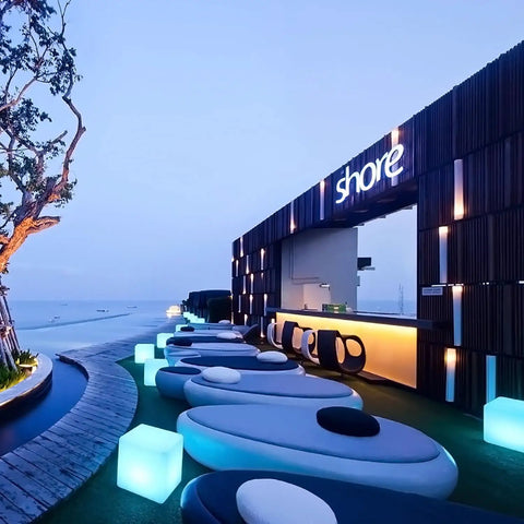 Outdoor lounge setting with 16 Inch LED Cube Chair Light With 16 RGB Colors Glow Cube Seat near shore bar at twilight