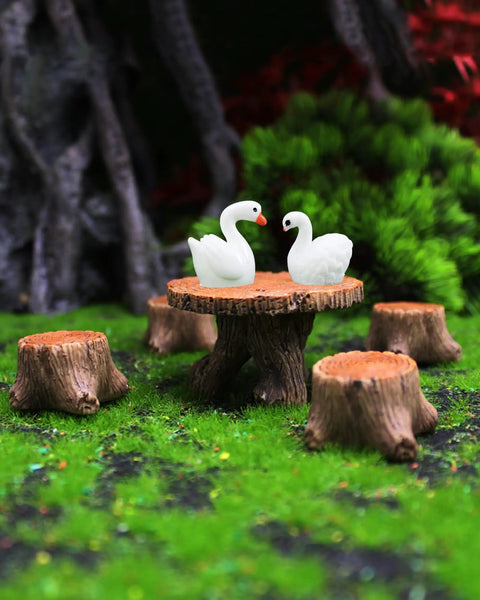 Totally Adorable Miniature Fairy Garden Furniture Set With Resin Table And Four Stump Seats displayed with swan figurines on a grassy landscape.
