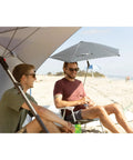 Two men on the beach under Versa-Brella SPF 50+ Adjustable Umbrella With Universal Clamp For On-The-Go Shade, regular size gray.