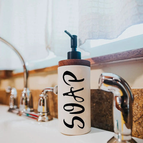 Soap dispenser on bathroom sink next to faucets.