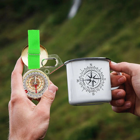 Multi-Use Finger Compass For Hiking And Orienteering held next to a mug with compass design