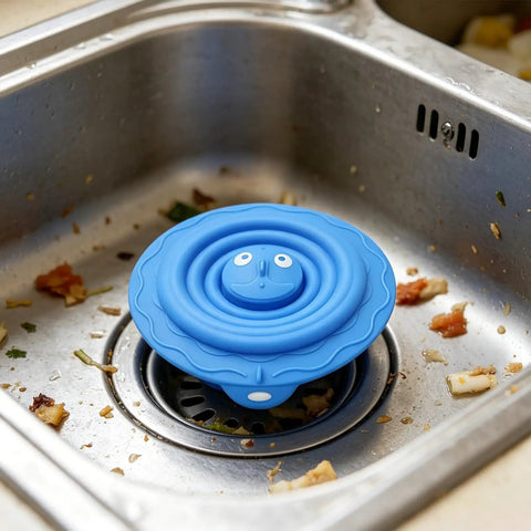 Drain Unclogger Flexible Bath Drain Cover Sealing Stopper in blue silicone resting in a kitchen sink with food debris.