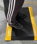 Person standing on black and yellow diamond plate anti-fatigue mat. Heavy Duty Anti Fatigue Mat 3 Ft By 6 Ft Diamond Plate Ergonomic Standing Floor Mat For Shops And Kitchens Cushioned Memory Foam Built For All Day Comfort Helps Relieve Back And Leg Soreness.