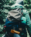 Person hiking with gear; Rugged Outdoor Survival Tool With Manual Drill Wrench And Scotch Eye Auger For Bushcrafting visible on bag