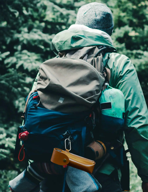 Person hiking with gear; Rugged Outdoor Survival Tool With Manual Drill Wrench And Scotch Eye Auger For Bushcrafting visible on bag