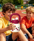 Two children on a track holding an 800ml Large Capacity Water Bottle With Handle For Sports And Hiking, cherry design visible.