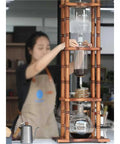 Big Batch Cold Brew Coffee Maker With Adjustable Stainless Steel Dripper And Roomy Borosilicate Glass Carafe in use on a wooden stand.