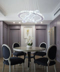 Dimmable LED Three-Ring Chandelier With Crystal Accents And Stainless Steel Pendant Light hanging over a dining table.
