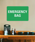 Emergency First Aid Sign For Outdoor Use 8 By 12 Inch Wall Decor For Home Office Shop Warehouse Factory Workplace Storage Zone Marker Plaque High Visibility Aluminum Notice With Bold Text For Clear Readability shown on wall above wooden shelf with bottles and cups.