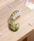 Delicate Lily Of The Valley Brooch For Women Featuring Tiny Bell Shaped Petals Lightweight Floral Pin on wooden surface.