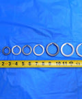 Top Shelf Bulk Lot Of Eight Precision Milling Machine Arbor Spacers For Your Shop Rig One Inch To One Nine Sixteenths Inside Diameter, metal spacers on blue background with tape measure.