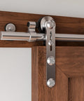 Close-up view of Stainless Steel Sliding Barn Door Hardware Kit 6 Foot, Smooth Quiet Operation, Easy Install, Heavy Duty Track For 36 Inch Single Wood Door, Anti Rust Satin Brushed Finish With Ball Bearing Rollers installed on wooden door.