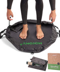 Person standing on wetsuit changing mat with box and bag, featuring Wetsuit Changing Mat And 2 In 1 Gear Bag With 5000X Waterproof Tech.