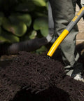 Heavy-Duty 10-Tine Bedding Fork With 48-Inch Hardwood Handle And Cushioned End Grip, in use moving soil in a garden.