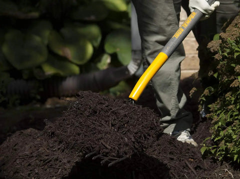 Heavy-Duty 10-Tine Bedding Fork With 48-Inch Hardwood Handle And Cushioned End Grip, in use moving soil in a garden.