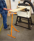 Person using D4800 Roller Stand With 12 Inch Ball Bearing Roller supporting a board in a workshop, orange finish visible.