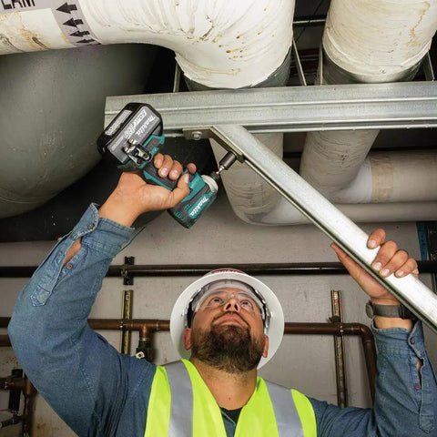Worker using impact driver to secure metal frame, wearing safety gear.