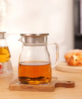 One Touch Glass Teapot 27 Oz 800 Ml Glass Tea Kettle With Stainless Steel Filter Lid on a wooden table with tea inside.