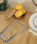 Heavy Duty No Burn Bowl Gripper Slick Stainless Steel Heat Resistant Pot Tongs Non Slip Dish Lifter on a wooden counter with lemons.