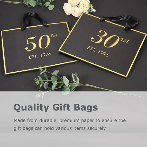 Black and gold 50th and 30th gift bags on a table with green leaves and flowers, featuring "Quality Gift Bags" text.