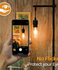 Hand holding smartphone with 4 Pack Vintage LED Edison Bulbs 60W Equivalent, 6W ST58 2700K Warm White in lamp fixture, clear glass
