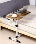 Slick Rolling Laptop Desk With Totally Adjustable Height And Easy Tilt Panel Super Sturdy Over Bed And Couch Cart For Working Or Hanging Out Plus 360 Degree Swivel Base next to a bed with a laptop and coffee cup.