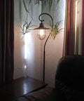 58 Inch Industrial Nautical Floor Lamp With Hanging Cage Shade, Brushed Pewter Finish in living room setting, next to couch and table