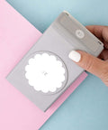 Hand holding 2.25 Inch Scalloped Circle Punch for Scrapbooks and Card Making, Large White Craft Punch against pastel papers