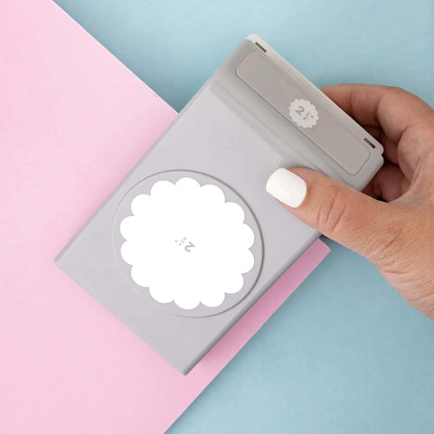 Hand holding 2.25 Inch Scalloped Circle Punch for Scrapbooks and Card Making, Large White Craft Punch against pastel papers