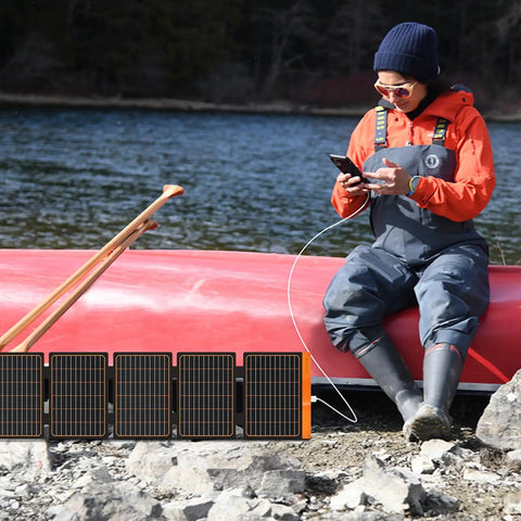 Person using 60W Portable Solar Panel Charger With PD3.0 USB C QC3.0 USB A And DC Output Foldable IP67 Waterproof Emergency Camping Power For Small Power Stations Grab And Go Phones Tablets And Power Banks on a canoe trip.