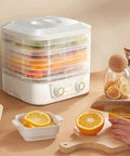 Big League Food Dehydrator Machine With Six Stackable Trays For Candy Snacks Beef Jerky Herbs on kitchen counter with sliced oranges.