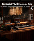 K7 DAC Headphone Amplifier for desktop gaming and HiFi music setup on a wooden desk with speakers and keyboard in a home environment.