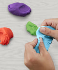Massive Bulk Modeling Compound With Twelve Four Ounce Cans Packing A Knockout Array Of Jewel Tones Absolutely Perfect For Kid Safe Arts Projects And Creative Crafting Vibes. Hands molding blue, orange, green, and purple modeling clay.