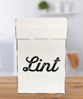 Front view of Vintage Shabby Chic Enamel Lint Bin With Magnetic Back, Retro Farmhouse Style, sitting on wooden counter.