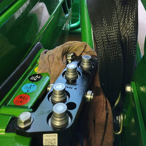 Side view of six 3/4-inch SAE hydraulic quick-connect couplers with dust caps on a green skid-steer valve block.