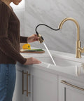 Modern Single Hole Kitchen Faucet With Slick Pull Down Sprayer Brushed Gold Finish in action with a woman preparing food.