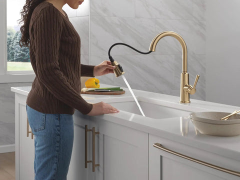Modern Single Hole Kitchen Faucet With Slick Pull Down Sprayer Brushed Gold Finish in action with a woman preparing food.