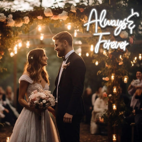 Wedding couple under floral arch with 'Always & Forever' neon sign glowing, surrounded by hanging lights in outdoor evening ceremony.