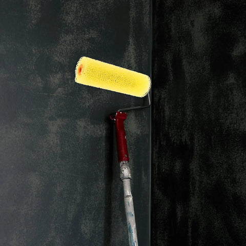 10 Piece Pack of Heavy Duty Sponge Paint Roller Sleeves on a roller handle painting a dark wall surface.
