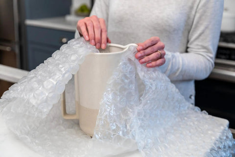 Person wrapping a ceramic jug with Heavy Duty Large Bubble Cushioning Wrap For Moving And Shipping, 60 Ft Perforated Bubble Roll.