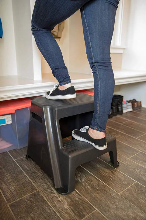 Person stepping on 2 Step Molded Plastic Step Stool Lightweight with Slip Resistant Treads and Non Slip Feet Ideal for Kitchen Bathroom Office or Garage Easy Carry with Cutout Handles Compact and Durable Amazon Exclusive