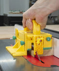 Hand holding Kickback Buster 3D Push Block With Gravity Heel Kit For Table Saws on cutting wood at a router station.