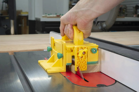 Hand holding Kickback Buster 3D Push Block With Gravity Heel Kit For Table Saws on cutting wood at a router station.