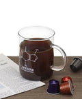 Glass mug from 2 Pack 16 Oz Caffeine Beaker Mug Set on desk with coffee pods, showing caffeine molecule design, chemistry-themed.