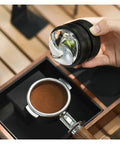 Pro Level Espresso Coffee Distributor And Tamper Set 58.35mm in hand above a portafilter with ground coffee on a wooden surface.