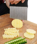 Front view of crinkle cutter with black handle and stainless steel wavy blade slicing potato on a wooden board