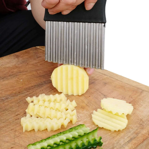 Front view of crinkle cutter with black handle and stainless steel wavy blade slicing potato on a wooden board