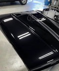 Car hood, top-down view, high-gloss black paint with reflections.
