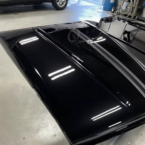 Car hood, top-down view, high-gloss black paint with reflections.